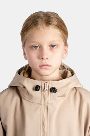 Child wearing a beige hooded jacket on a light background