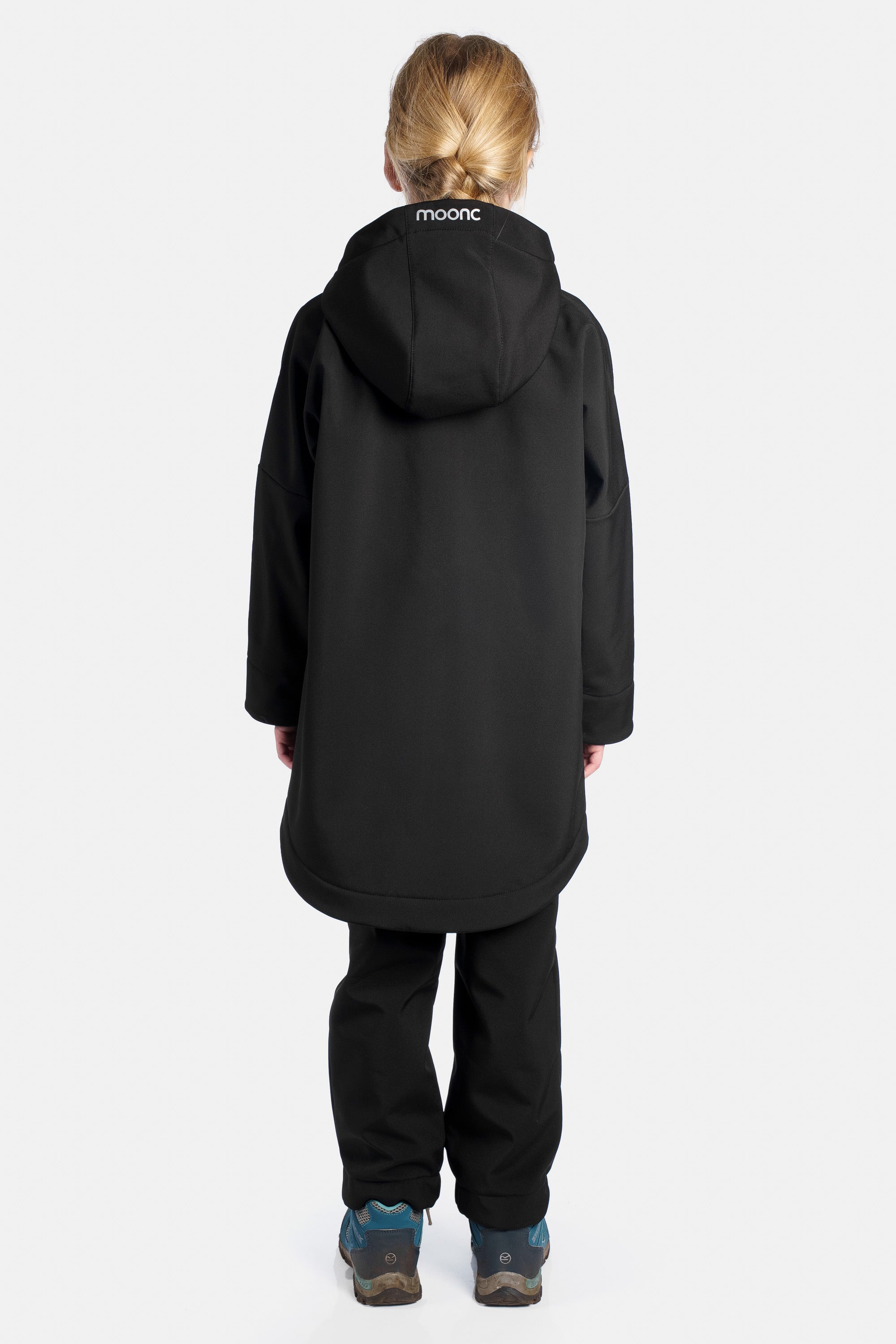 Girl wearing a black coat with a visible brand logo on the back, standing against a white background.